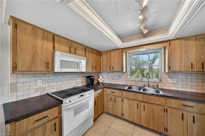 Kitchen featuring wood-finish cabinetry, dark countertops, a white tile backsplash, and a double basin stainless steel sink