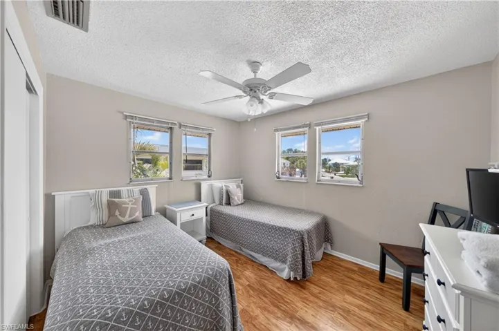 Bedroom featuring wood-finish flooring, two large windows, a ceiling fan with light, and light-toned wall paint