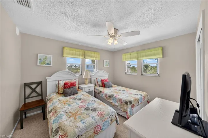 Carpeted bedroom featuring two twin beds with white headboards, a ceiling fan, and two windows with light green valances
