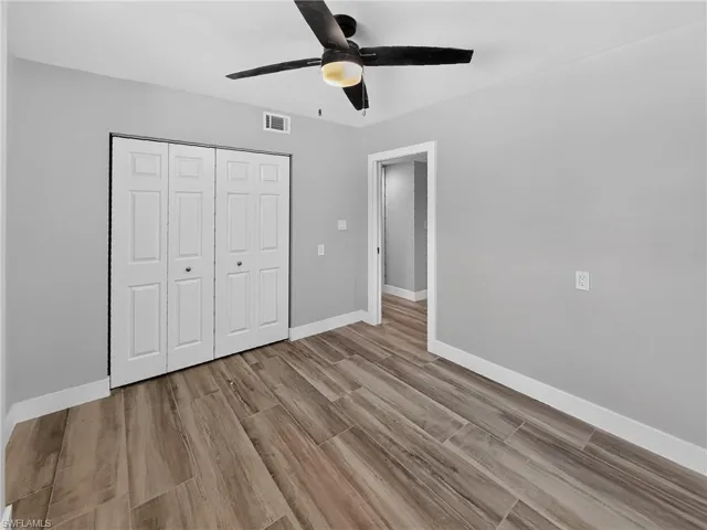 Room featuring wood-finish flooring, a ceiling fan with integrated lighting, and light gray wall paint