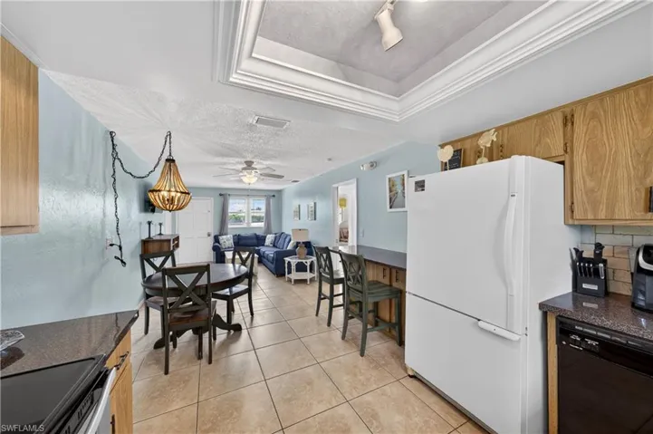 Kitchen and dining area featuring tile flooring, wood cabinetry, dark countertops, a tile backsplash, and an integrated breakfast bar