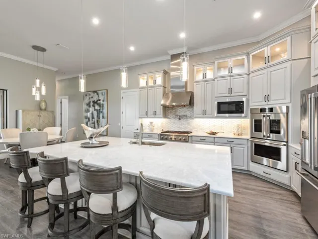 Kitchen with decorative light fixtures, a kitchen breakfast bar, tasteful backsplash, stainless steel appliances, and crown molding