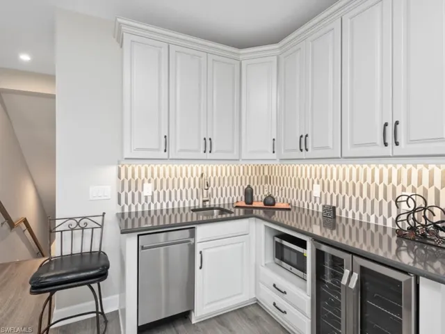 Indoor wet bar with wine cooler, appliances with stainless steel finishes, white cabinets, light wood finished floors, and dark stone counters