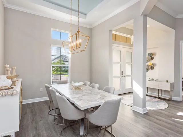 Dining area featuring crown molding, french doors, dark wood finished floors, a chandelier, and a raised ceiling