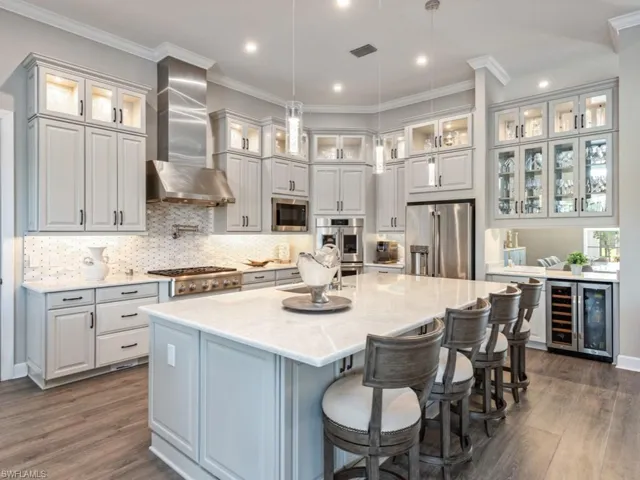 Kitchen featuring ornamental molding, a breakfast bar area, wine cooler, light stone counters, and appliances with stainless steel finishes