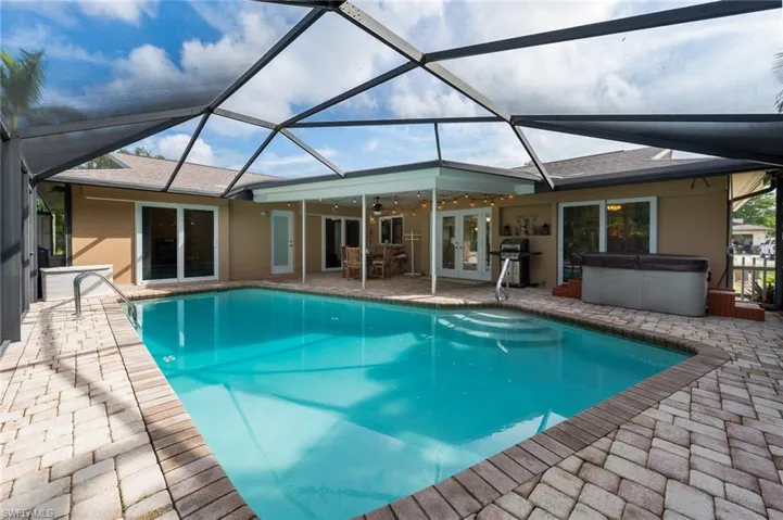 View of pool with a covered patio, a hot tub, screened enclosure, ceiling fan, and pass-through window to the kitchen.