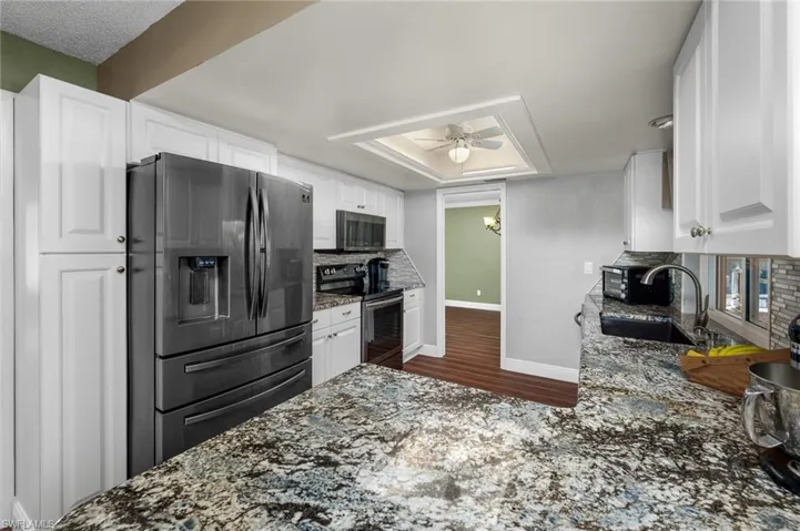 Kitchen featuring granite counters, white cabinetry, ceiling fan, and stainless-steel appliances.