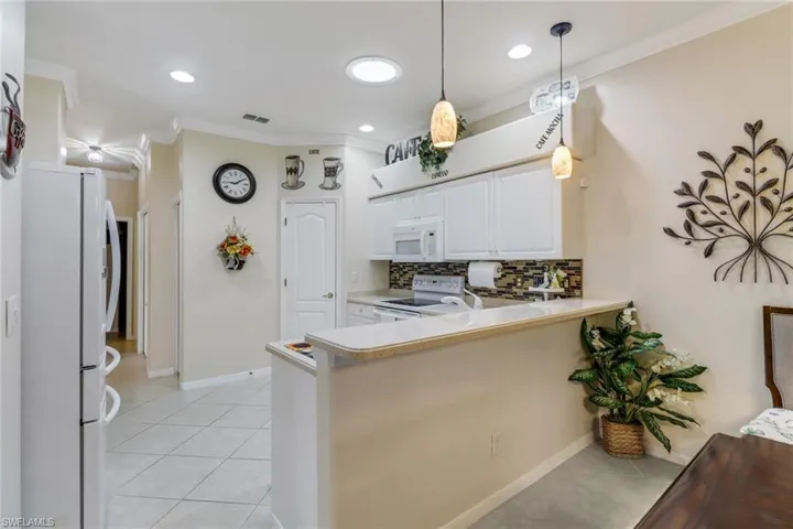 Kitchen with white appliances, ornamental molding, tasteful backsplash, light tile patterned floors, and white cabinetry