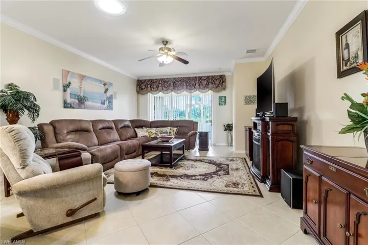 Living room with ceiling fan, ornamental molding, and light tile patterned floors