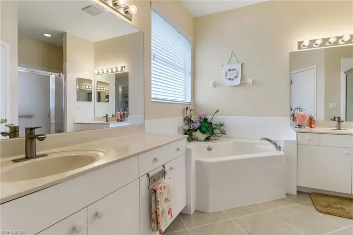 Full bathroom featuring tile patterned flooring, two vanities, a stall shower, and a garden tub