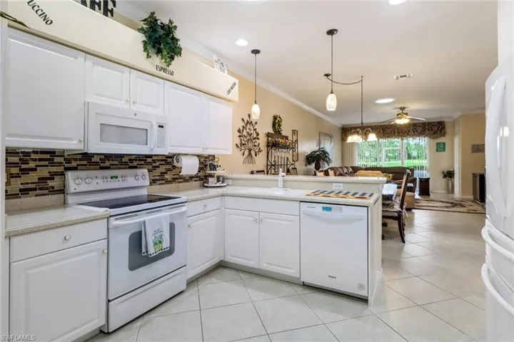 Kitchen featuring white appliances, ornamental molding, a peninsula, backsplash, and white cabinets