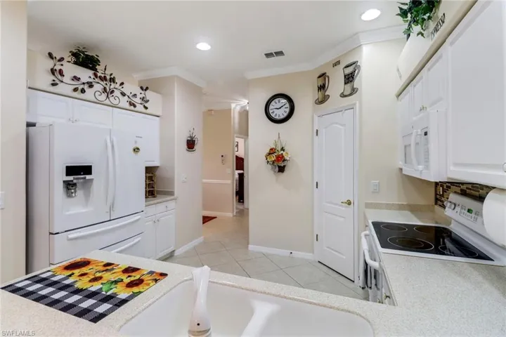 Kitchen with white appliances, light countertops, white cabinetry, backsplash, and recessed lighting