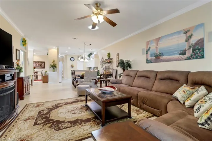 Living area featuring ceiling fan, crown molding, light tile patterned flooring, recessed lighting, and a chandelier