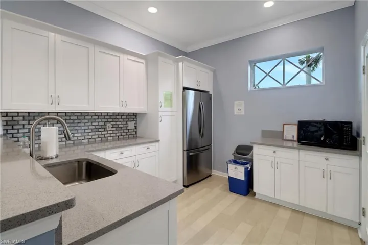 Kitchen with freestanding refrigerator, tasteful backsplash, black microwave, light stone counters, and white cabinets