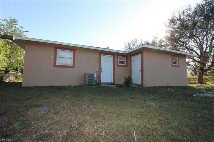 Rear view of property with cooling unit and a lawn
