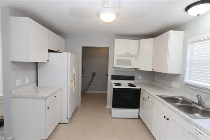 Kitchen with white cabinetry, white appliances, light tile patterned flooring, and sink