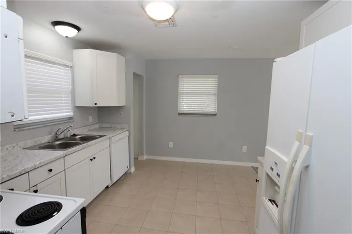 Kitchen with white appliances, light stone countertops, sink, and white cabinets