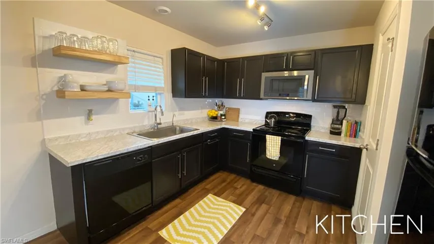 Kitchen with black appliances, dark cabinetry, dark wood-style flooring, and open shelves