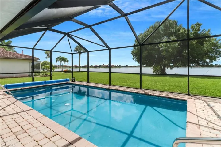 View of swimming pool with glass enclosure, a lawn, and a water view