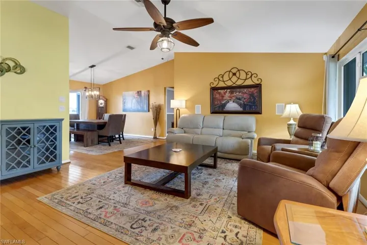 Living room featuring ceiling fan with notable chandelier, vaulted ceiling, and light hardwood / wood-style floors