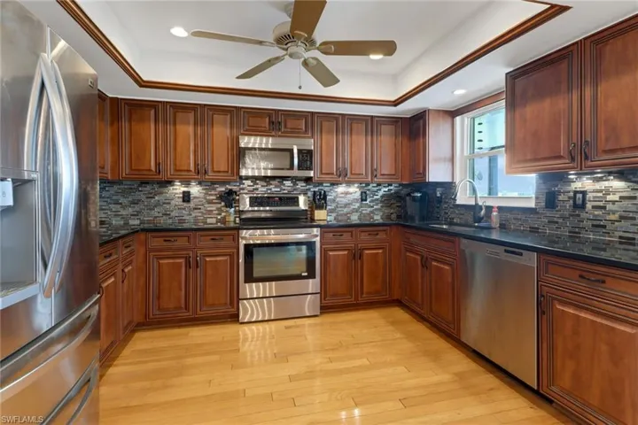 Kitchen featuring dark stone countertops, stainless steel appliances, sink, ceiling fan, and decorative backsplash