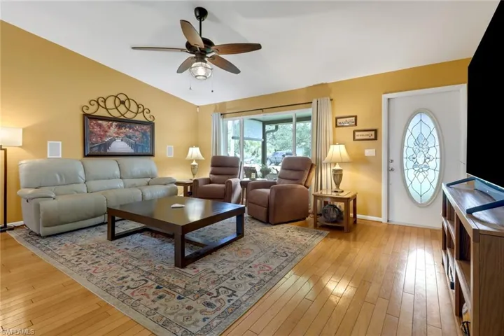 Living room with ceiling fan, light wood-type flooring, and vaulted ceiling