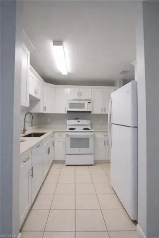 Kitchen with white cabinets, white appliances, light tile patterned floors, and light stone counters