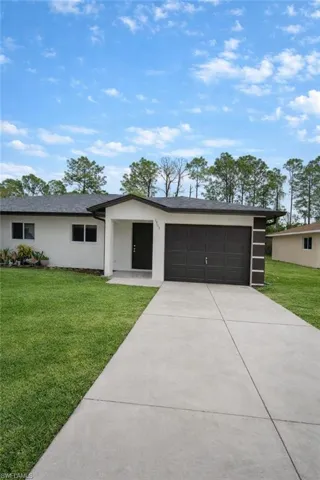 View of front facade featuring a front yard, driveway, an attached garage, stucco siding, and roof with shingles
