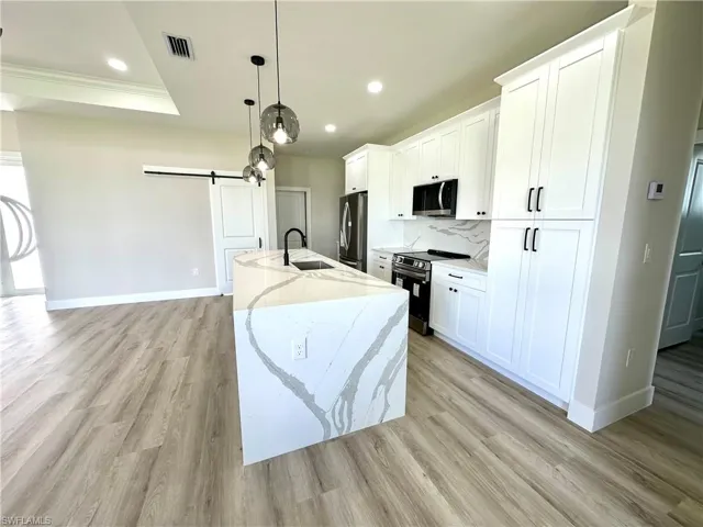 Modern kitchen featuring a waterfall-edge island with integrated sink, sleek pendant lighting, white shaker cabinetry with matte black hardware, and wood-finish flooring