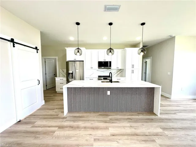 Modern kitchen featuring a waterfall island with a slatted base, white shaker cabinetry, stainless steel appliances, and wood-finish flooring