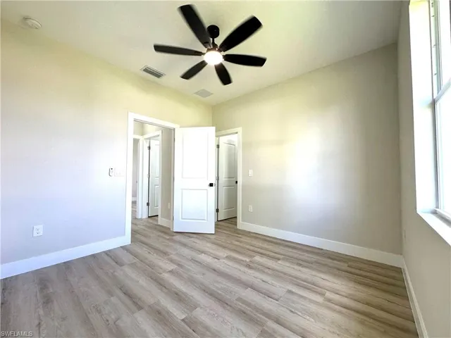 Bright interior room featuring wood-finish flooring, a contemporary ceiling fan, baseboard molding, and multiple doorways with white panel doors