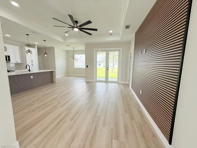 Open-concept living space featuring wood-finish flooring, a contemporary slat wall, and a tray ceiling with a modern ceiling fan