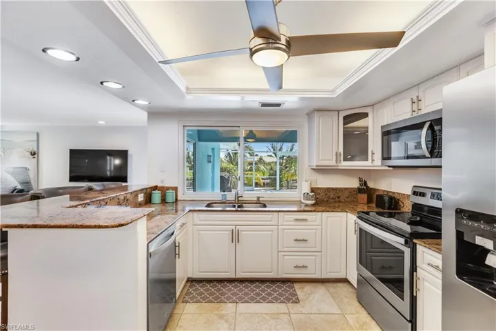 Kitchen with ceiling fan, dark stone countertops, a raised ceiling, and appliances with stainless steel finishes