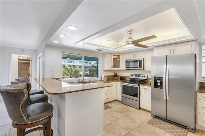Kitchen with light tile patterned floors, ceiling fan, a raised ceiling, stainless steel appliances, and kitchen peninsula