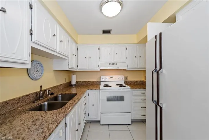 Kitchen featuring white appliances, white cabinets, granite stone counters, and light tile patterned floors