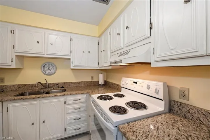 Kitchen featuring white electric range, white cabinets, and light granite stone counters