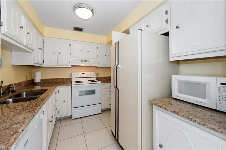 Kitchen with white appliances, granite stone countertops, white cabinetry, and light tile patterned floors