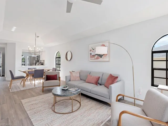 Living room featuring vaulted ceiling, hardwood / wood-style floors, plenty of natural light, and ceiling fan with notable chandelier