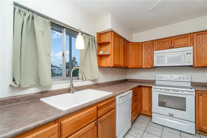 Kitchen featuring decorative light fixtures, white appliances, sink, and light tile flooring