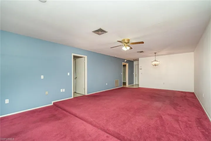 Carpeted empty room featuring ceiling fan with notable chandelier