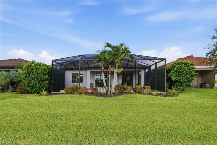 Expansive rear lawn featuring a screened lanai, mature landscaping, and an exterior of light-colored stucco