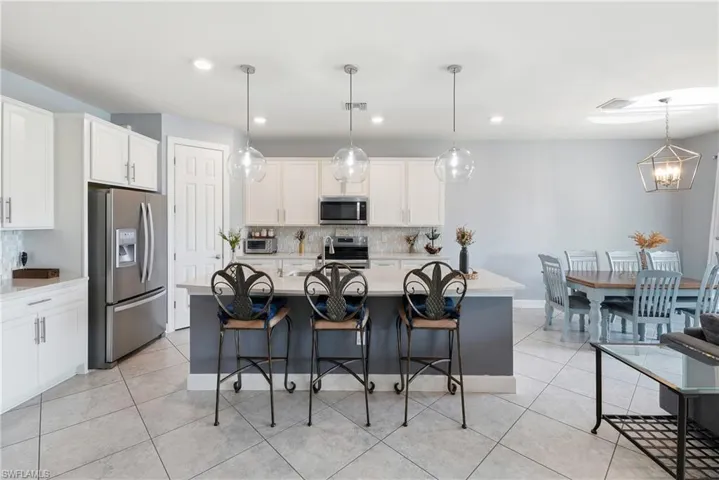 Open-concept kitchen and dining area featuring a central island, white cabinetry, stainless steel appliances, and tile flooring