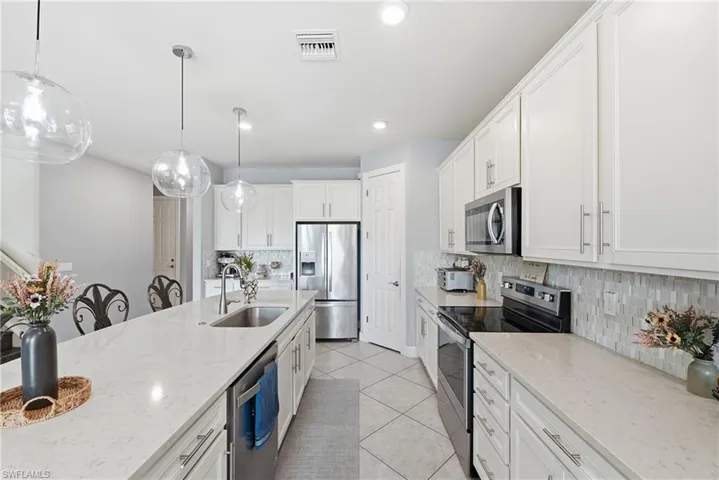 Kitchen featuring white cabinetry, stainless steel appliances, a long center island with an undermount sink, pendant lighting, and light-toned countertops