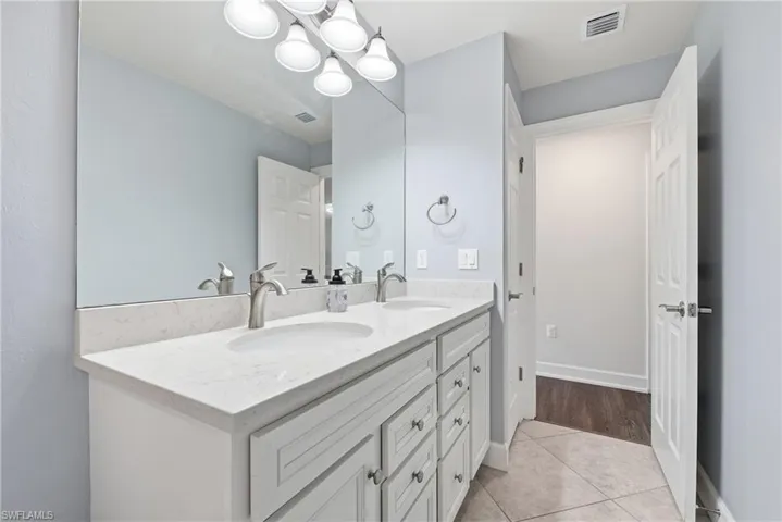 Bathroom featuring a dual-sink vanity with a light-toned countertop, integrated sinks, white cabinetry, and brushed nickel fixtures