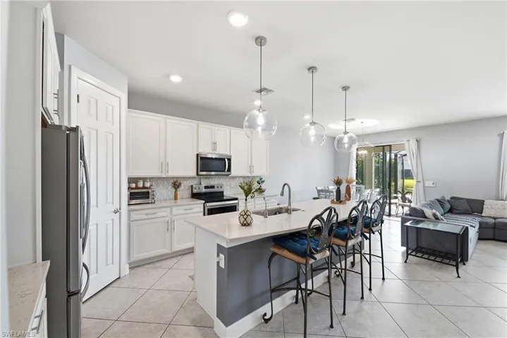 Open-concept kitchen featuring white cabinetry, stainless steel appliances, and a central island with a sink
