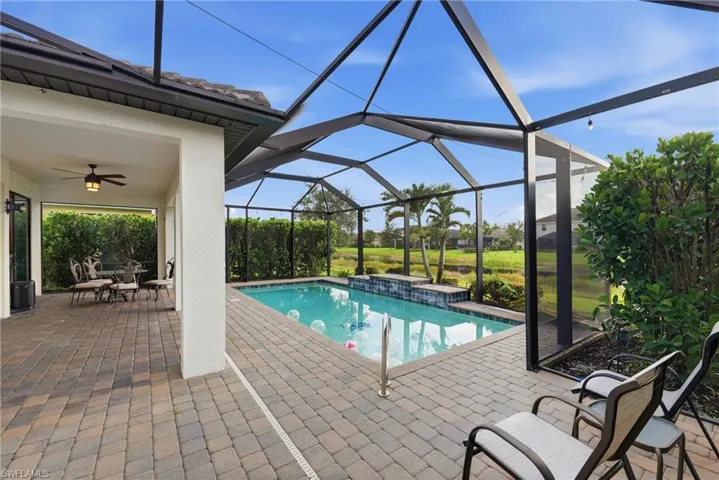 Screened lanai featuring a swimming pool with a waterfall, paver patio, covered outdoor living space with a ceiling fan, and lush landscaping