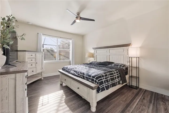 Spacious bedroom featuring a white wood bed frame, coordinating dresser and nightstands with ample storage, dark wood-finish flooring, ceiling fan with integrated lighting, and sliding glass doors providing natural light and access to outdoor space