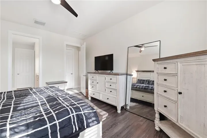 Spacious bedroom featuring hardwood flooring, white painted cabinetry with multiple drawers and storage, a flat-screen television mounted above a dresser, and coordinating furniture pieces