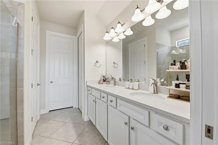 Spa-inspired primary bathroom featuring a dual-sink vanity with white cabinetry, quartz countertops, and polished nickel hardware