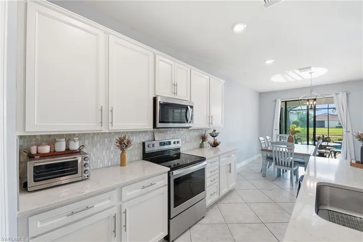Kitchen featuring white shaker cabinetry, stainless steel appliances, light-toned countertops, and a tile backsplash